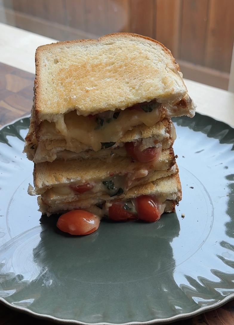 A stack of three grilled cheese sandwiches with melted cheese, tomatoes, and basil, served on a green plate.