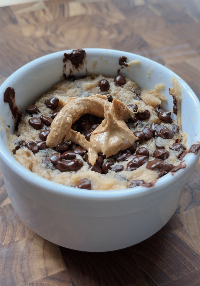A fluffy mug cake filled with chocolate chips and topped with peanut butter, served in a white ramekin on a wooden surface.