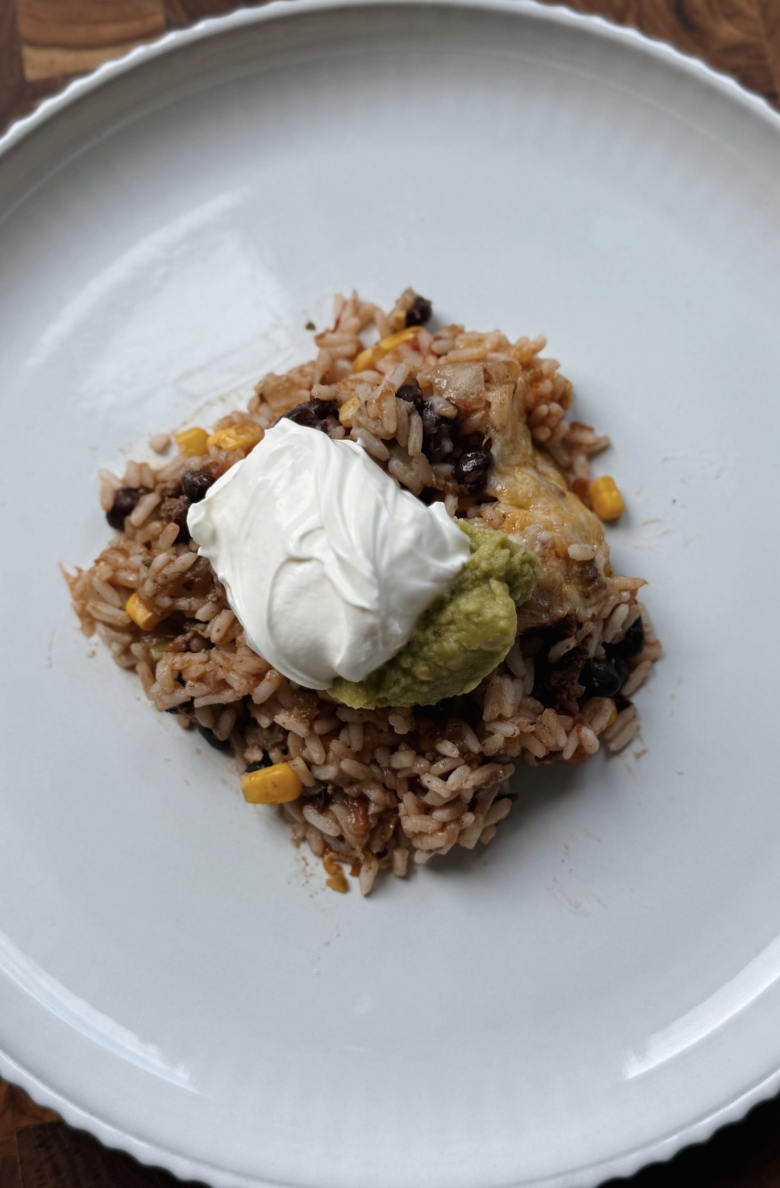 A plate with a serving of rice mixed with black beans and corn, topped with a dollop of sour cream and a spoonful of guacamole.
