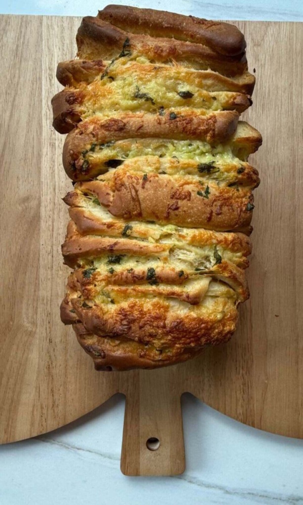 A cheesy, herb-filled pull-apart loaf on a wooden cutting board, golden and bubbling.