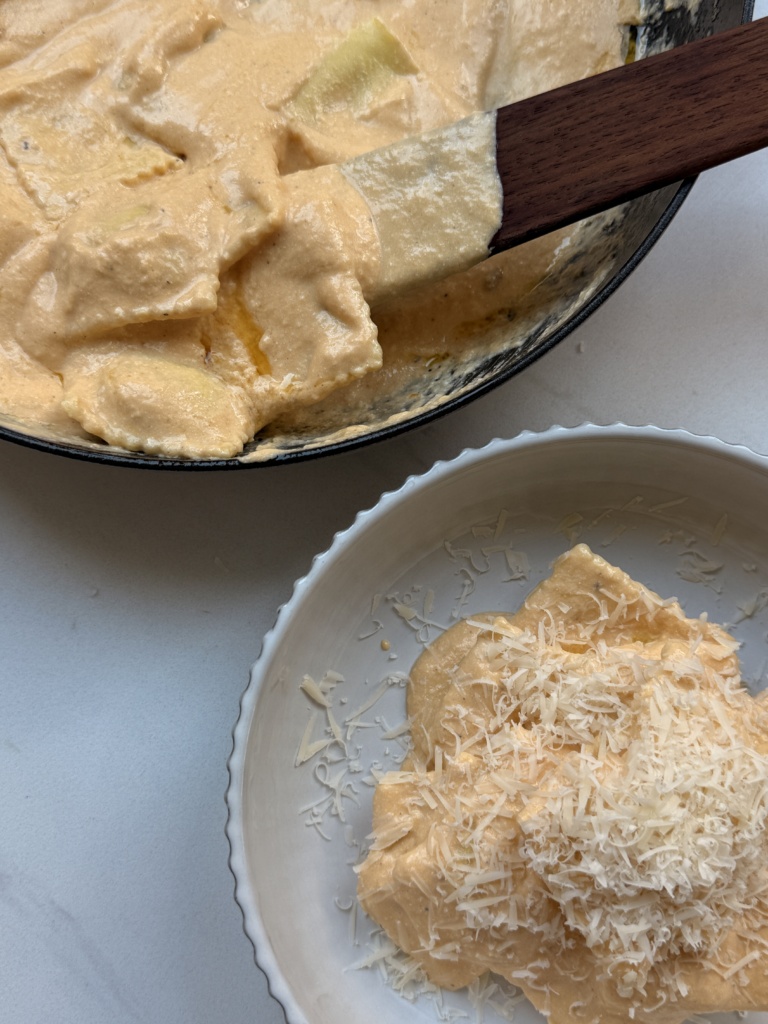 Overhead view of creamy butternut squash ravioli in a skillet with fresh sage and a golden sauce.