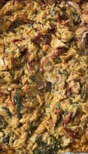 Creamy tuscan chicken orzo bake with spinach and sun dried tomatoes in a baking dish