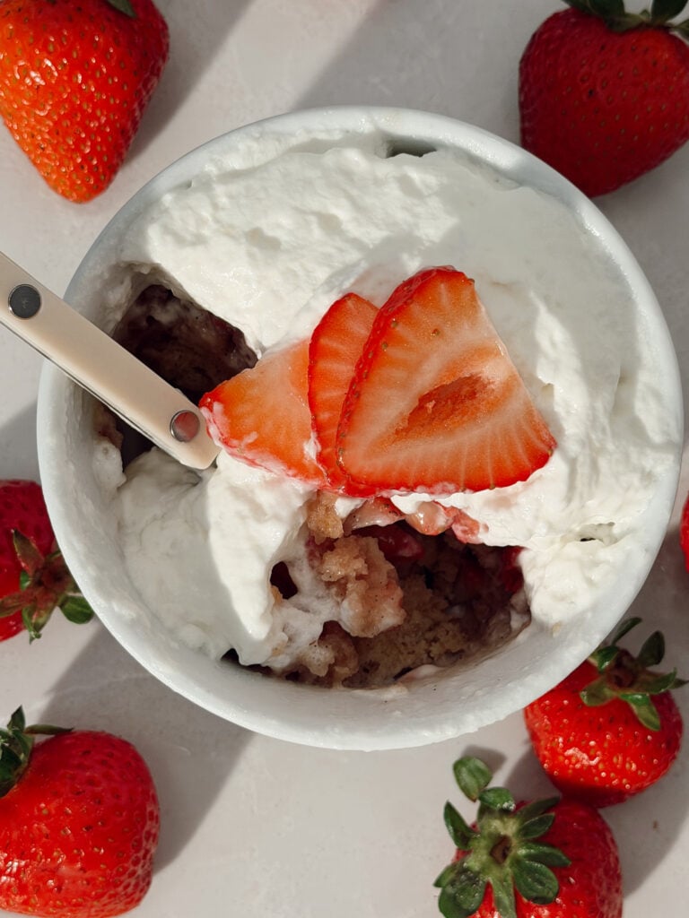 Strawberry shortcake mug cake topped with macerated strawberries and whipped cream